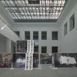 public preposition im Baukunstarchiv NRW. Ein heller Ausstellungsraum, mittig stehen Baugerüste mit Bannern.